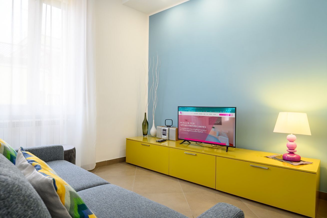 A modern living room with a sofa, a yellow cabinet, a television, and a lamp.
