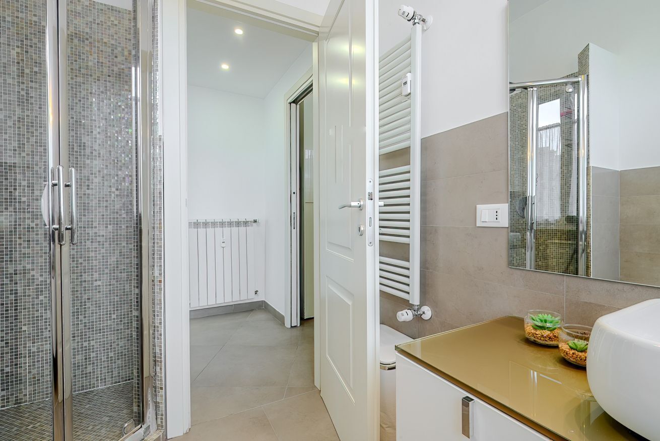 Une salle de bain moderne avec une douche à parois de verre, un meuble-lavabo blanc doté d’un plan de toilette doré et un grand miroir.