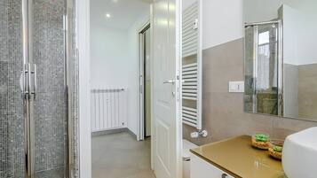 Une salle de bain moderne avec une douche à parois de verre, un meuble-lavabo blanc doté d’un plan de toilette doré et un grand miroir.