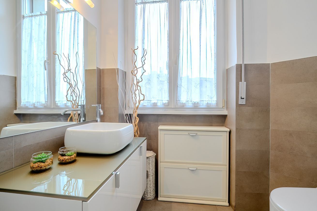 A modern bathroom with a large mirror, a white sink, a white toilet, and a small cabinet.