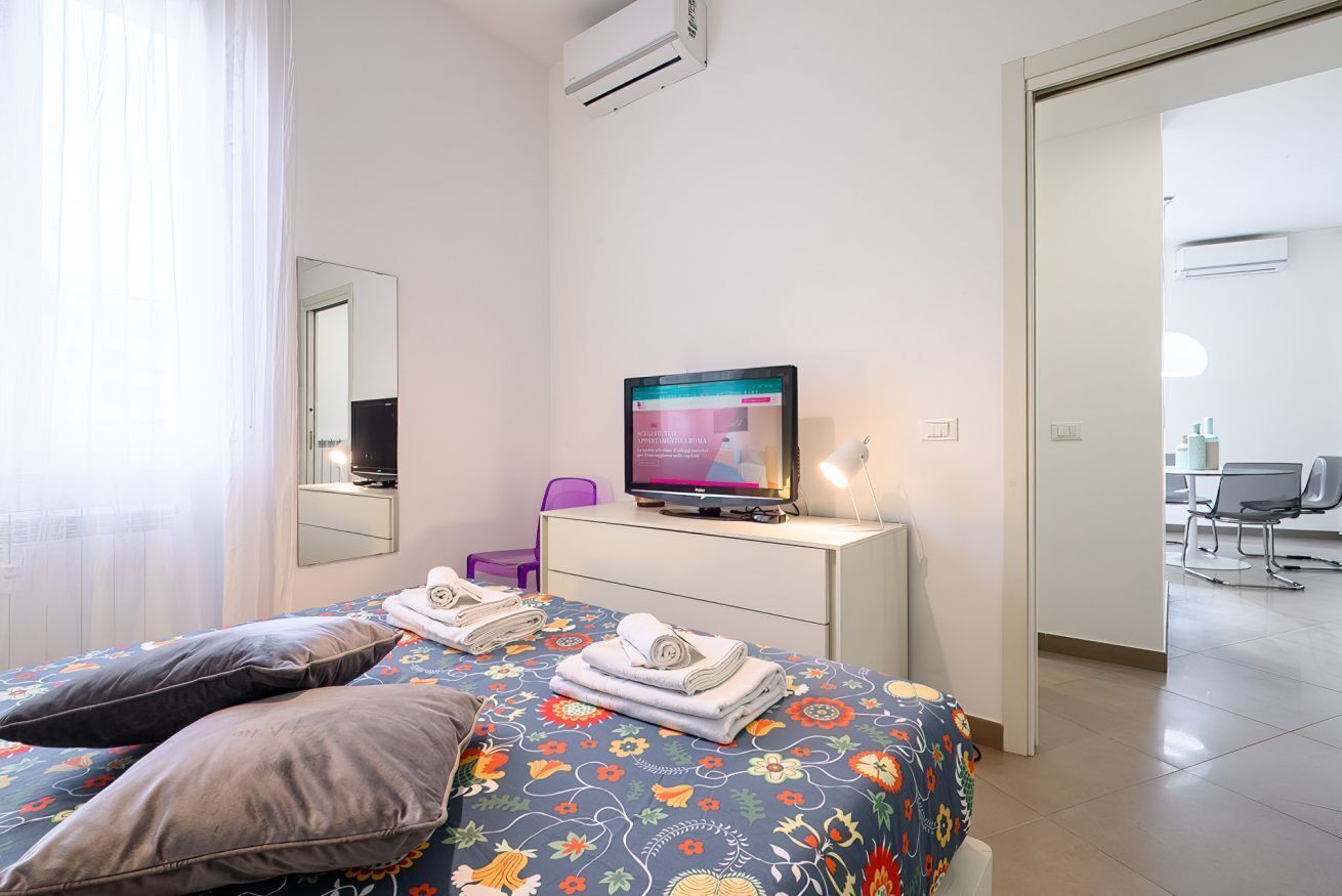 Une chambre d’hôtel avec un lit, une télévision, un bureau, une chaise et une salle de bain visible à travers une porte ouverte.