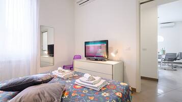 Une chambre d’hôtel avec un lit, une télévision, un bureau, une chaise et une salle de bain visible à travers une porte ouverte.