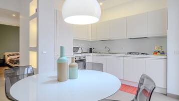 Une cuisine moderne avec des meubles blancs, une table ronde en verre et un luminaire suspendu.