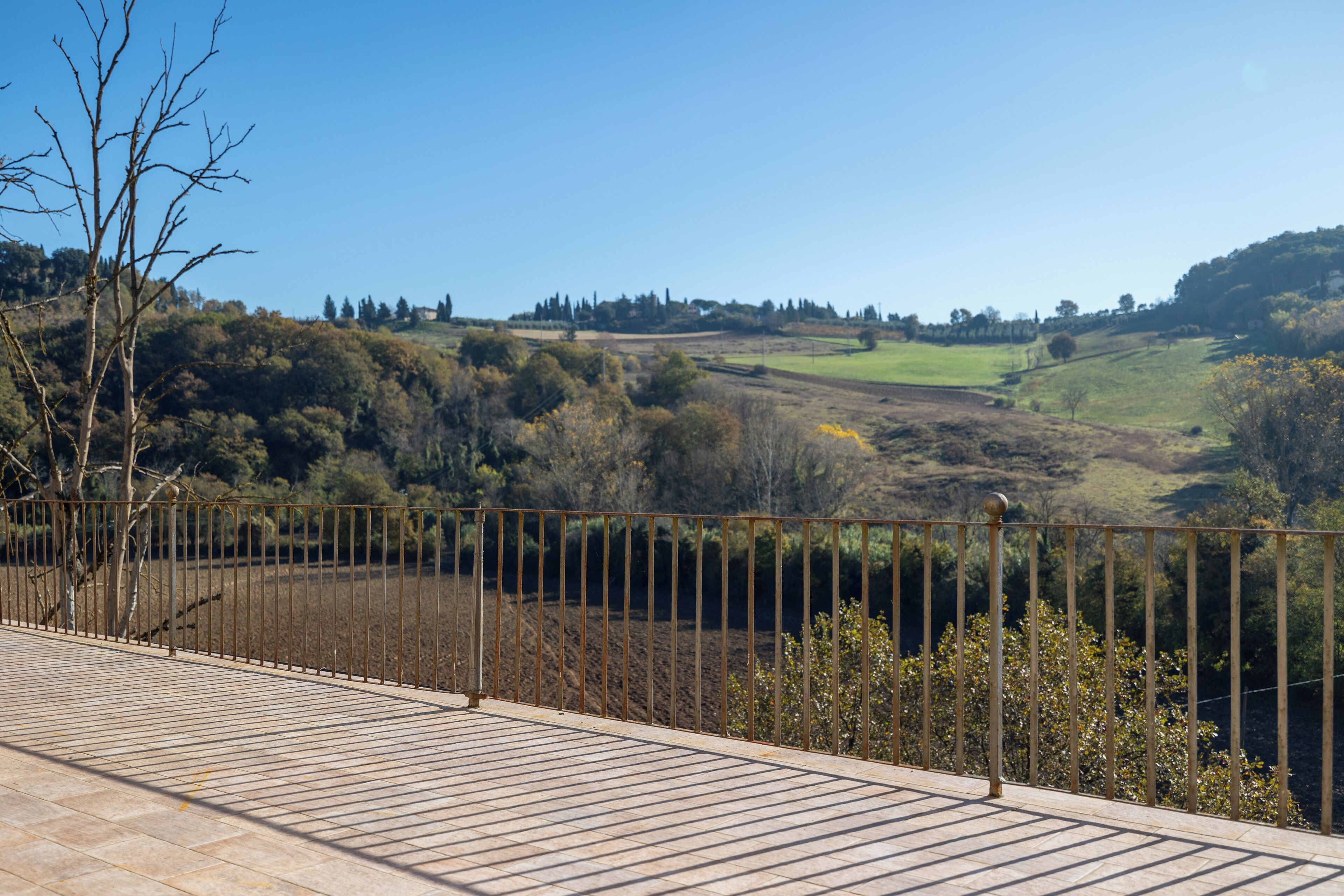 Una terraza con barandilla de metal que da a un paisaje montañoso con árboles y campos abiertos.