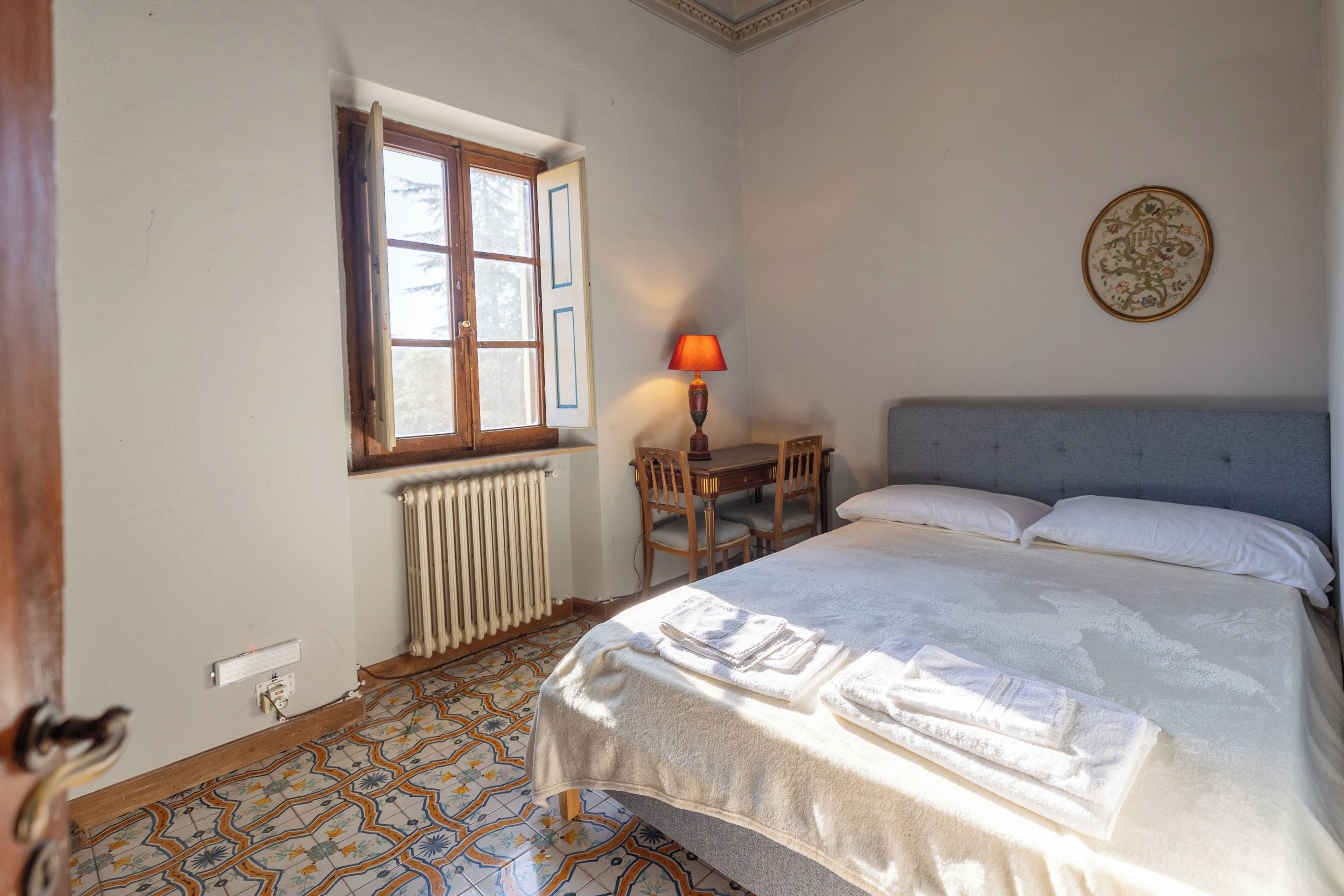 A bedroom with a bed, a table with chairs, a window, and a radiator.