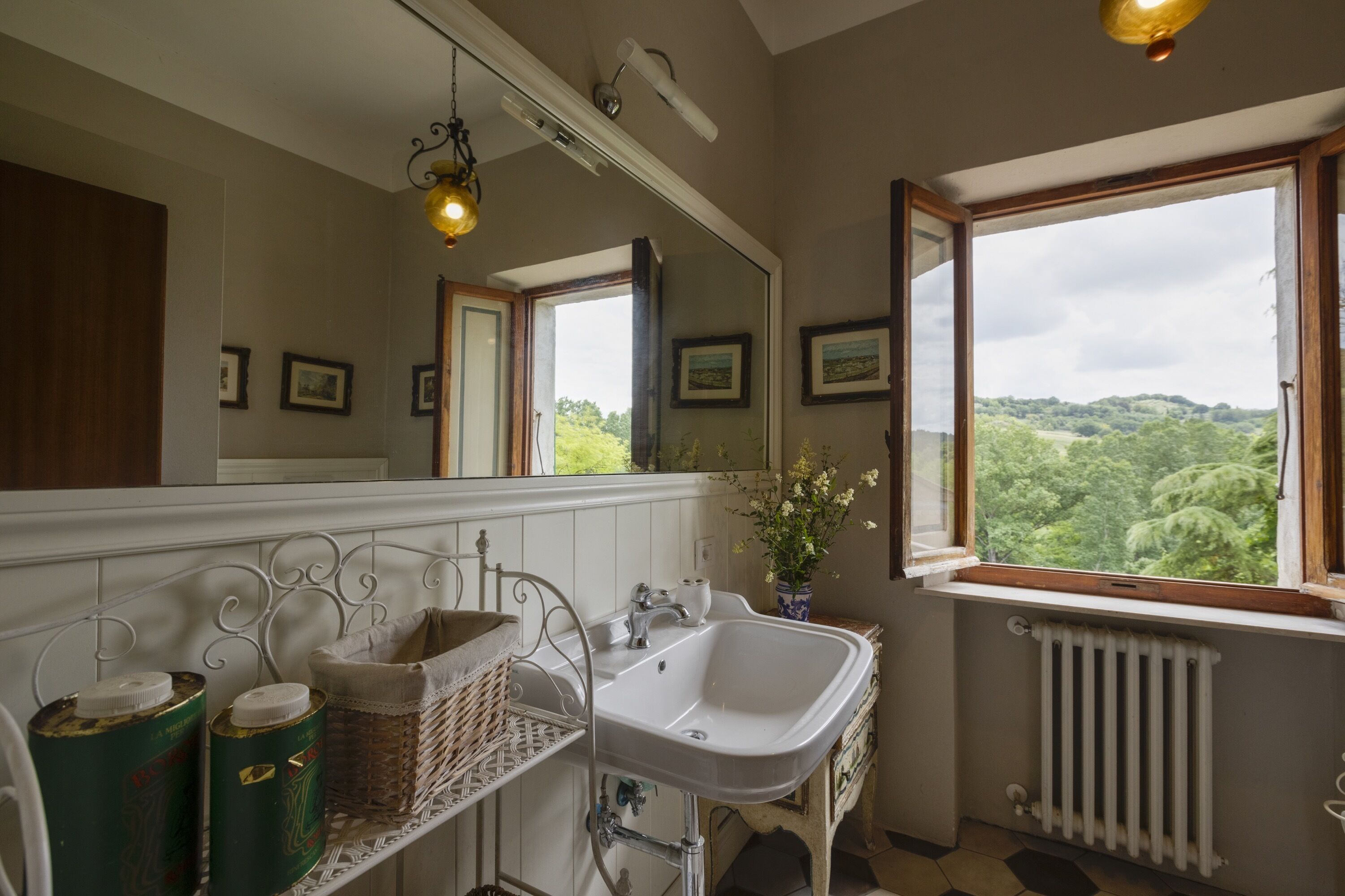 Une salle de bain avec un lavabo blanc, un miroir et une fenêtre donnant sur un paysage verdoyant.
