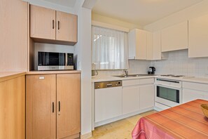 A compact kitchen with wooden cabinets, a microwave, a Bosch dishwasher, and a stove. - 2 bedroom accommodation in Wenduine (Wenduine)