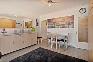 A modern kitchen with wooden cabinets, a dining table with chairs, a black rug, and a cityscape painting on the wall. - 1 bedroom accommodation in Blankenberge (Blankenberge)