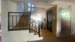 Un escalier avec une rampe métallique menant à l’étage supérieur, une porte avec une poignée et une vue sur l’extérieur à travers une porte vitrée.
