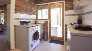 A compact kitchen with a washing machine, a small trash bin, and a sliding glass door leading to an outdoor area.
