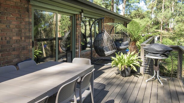 A wooden deck with a table and chairs, a hanging chair, and a grill.