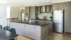 A modern kitchen with grey cabinets, a stainless steel refrigerator, and a wooden dining table with chairs.