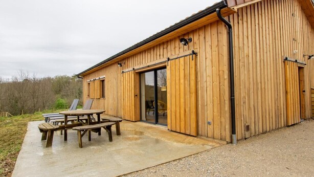 A wooden building with a large sliding door and a patio area with a table and benches.