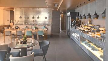 Un espace repas moderne avec des tables rondes, des chaises et un buffet proposant une variété de plats.