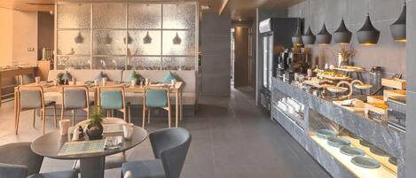 A modern dining area with round tables, chairs, and a buffet counter with various food items.