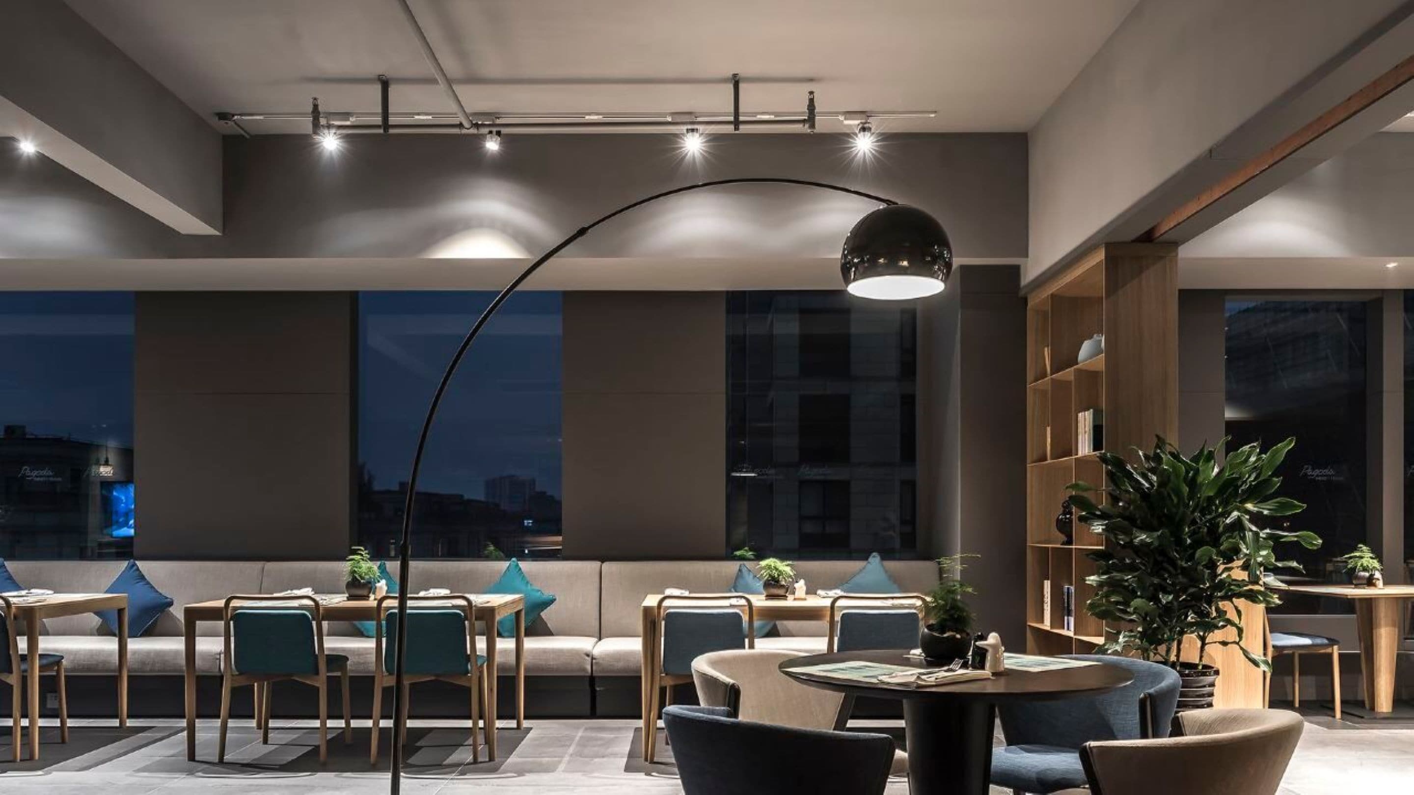A modern lounge area with seating and tables, large windows, and a curved ceiling light.