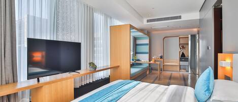 Una habitación de hotel moderna con una cama grande, un televisor de pantalla plana, un escritorio y un área de descanso con vista a la ciudad.
