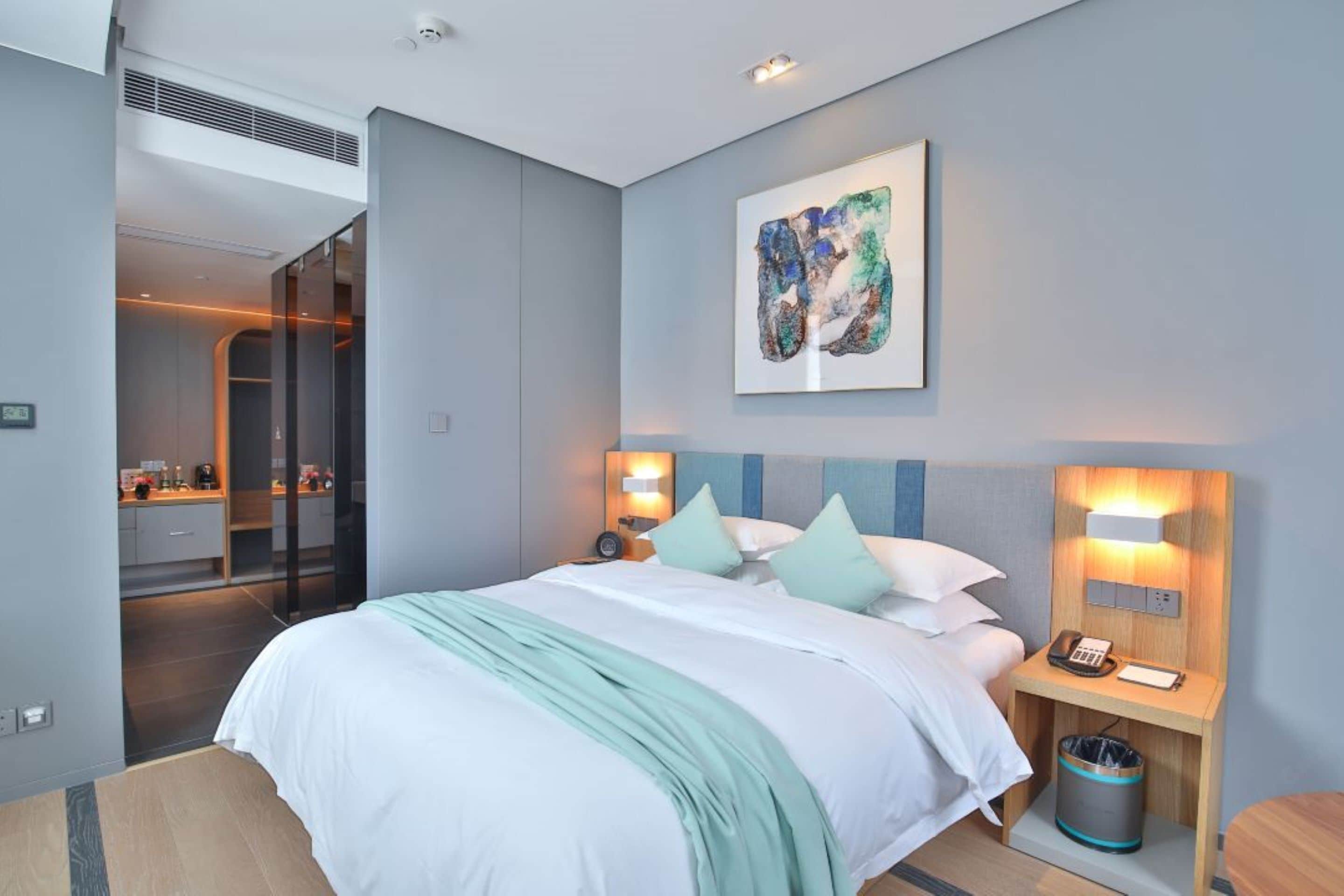 A modern hotel room with a large bed, bedside lamps, a painting, and a view of the bathroom.