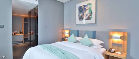 A modern hotel room with a large bed, bedside lamps, a painting, and a view of the bathroom.