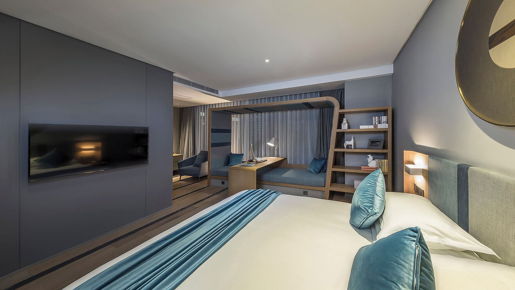 A modern hotel room with a large bed, a desk, a bookshelf, and a TV mounted on the wall.