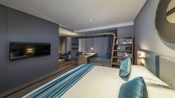 A modern hotel room with a large bed, a desk, a bookshelf, and a TV mounted on the wall.
