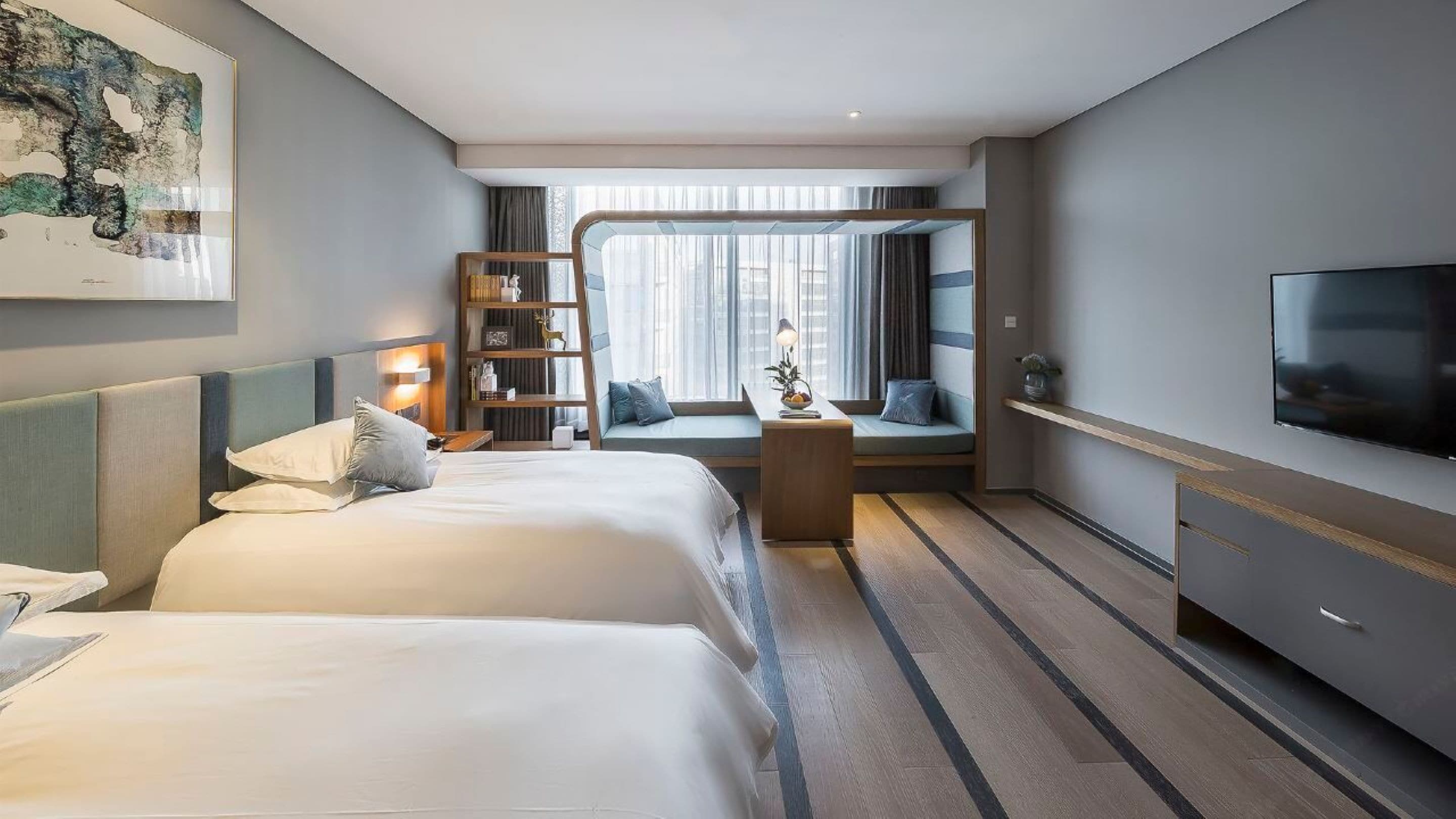 A hotel room with two beds, a seating area with a bookshelf, a TV, and a large window.