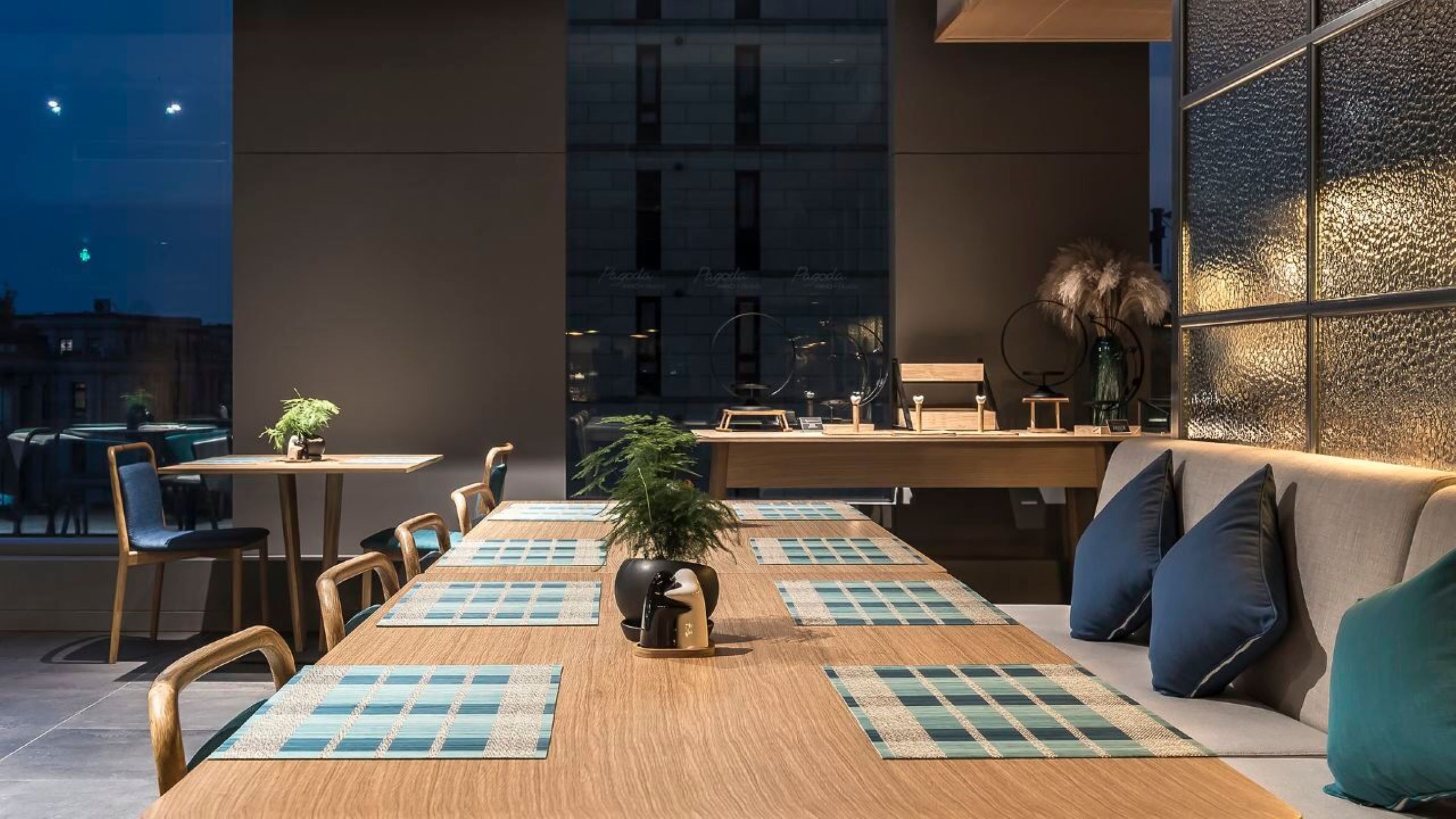 Un comedor moderno con una larga mesa de madera, individuales azules y un sofá con cojines.