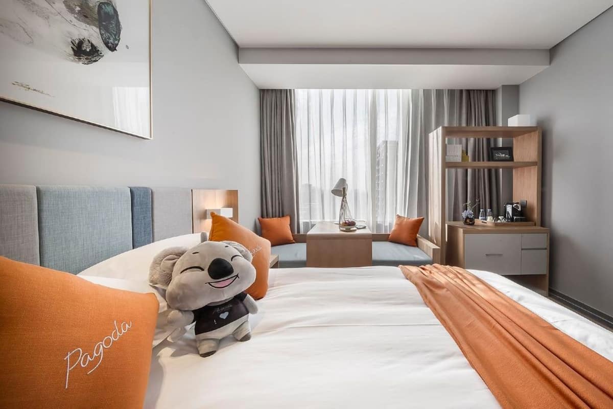 Ein Hotelzimmer mit einem Bett, einem Schreibtisch, einem Stuhl, einem Fernseher und einem Fenster mit Vorhängen.
