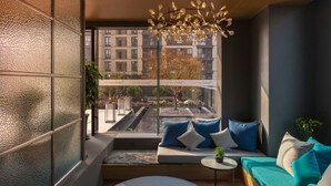 A modern interior with a sofa and a small table, a view of a cityscape through large windows, and a decorative light fixture.