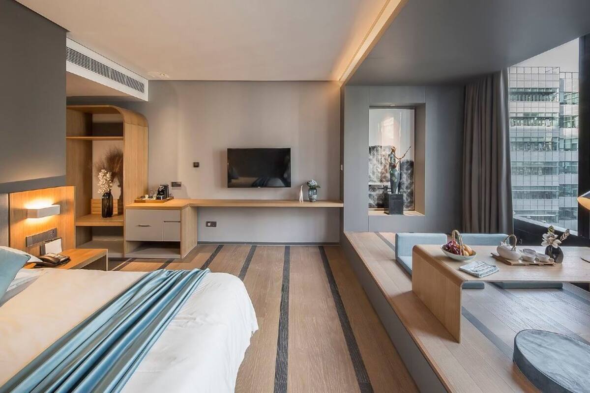 Ein modernes Hotelzimmer mit Bett, Schreibtisch, Fernseher und großen Fenstern mit Blick auf die Stadt.