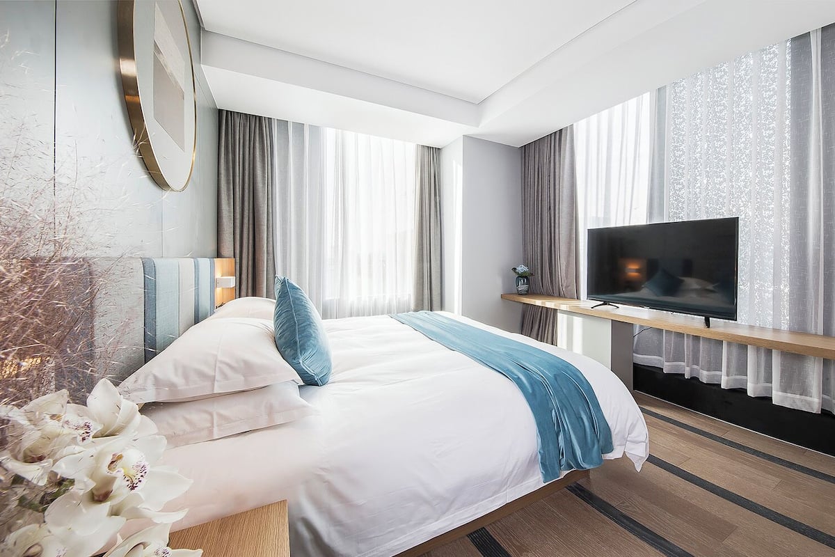 Ein modernes Hotelzimmer mit einem großen Bett, einem Fernseher und einer hölzernen Sitzbank.