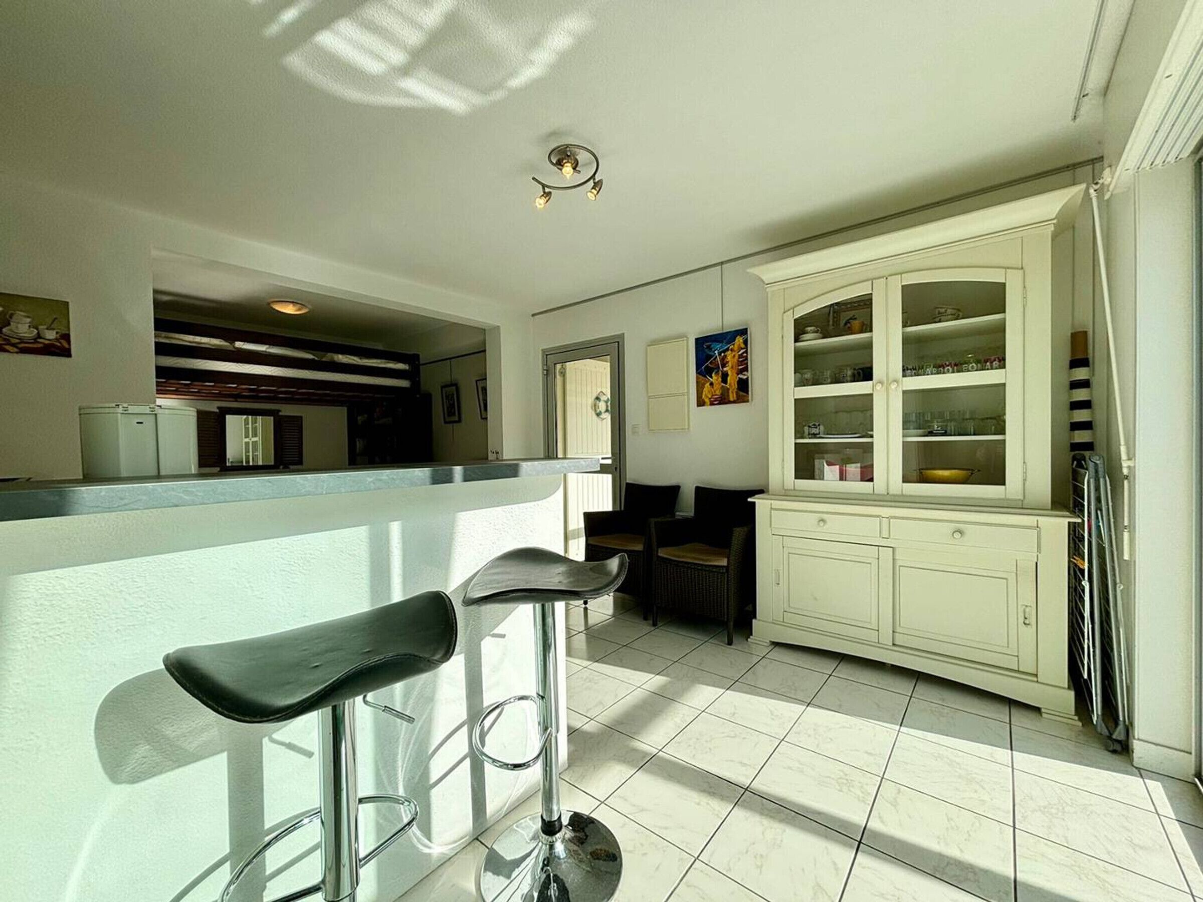 Een keuken met een bar, witte kastjes en een betegelde vloer.