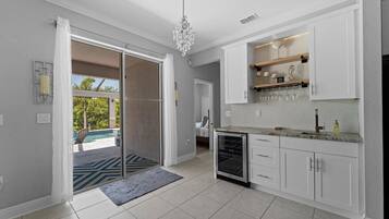 Une cuisine moderne avec des meubles blancs, un réfrigérateur à vin intégré et une vue sur l’espace piscine extérieur.