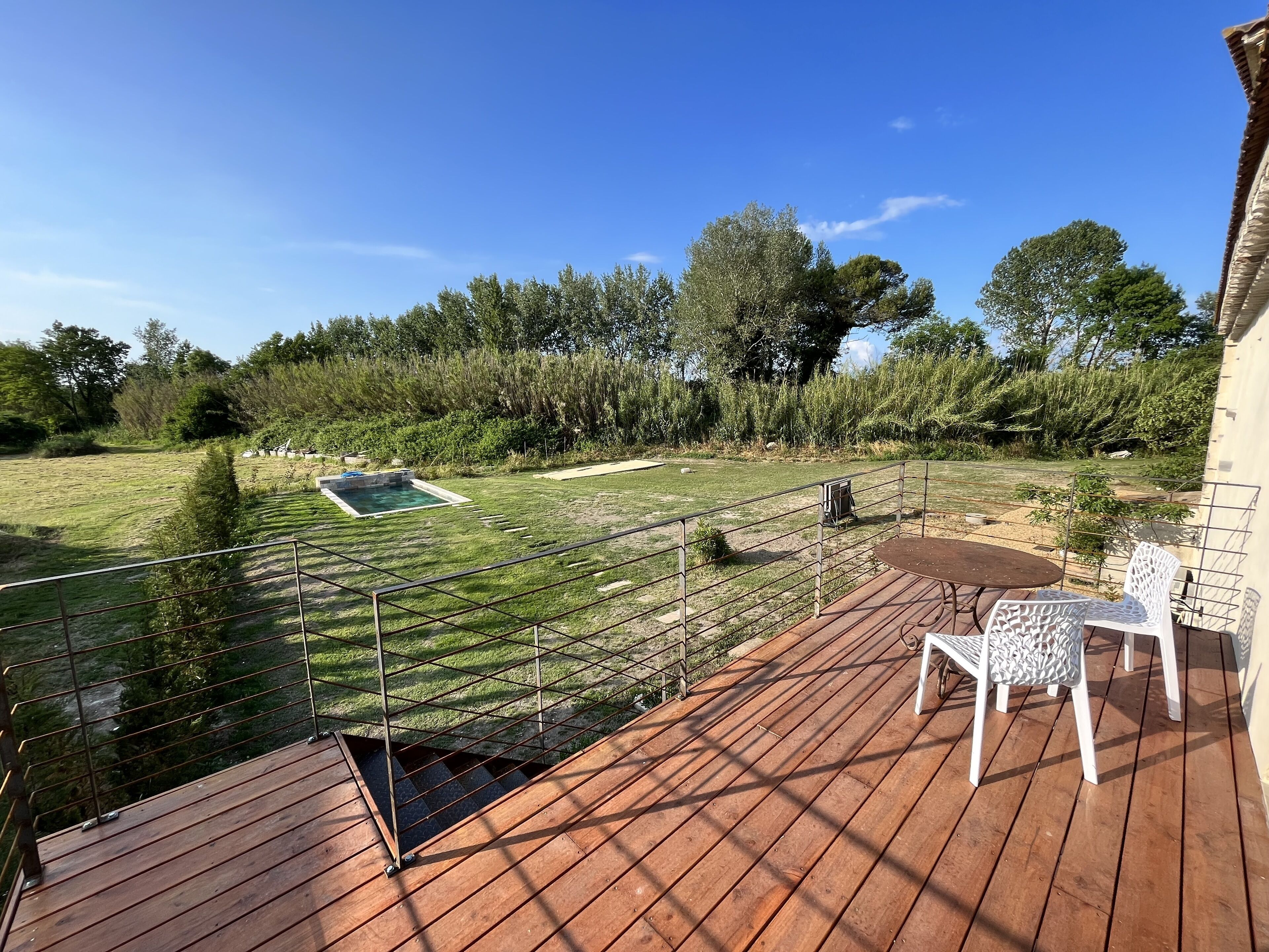 Una terraza de madera con mesa y sillas, una piscina pequeña y un patio cercado con árboles.