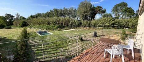 Una terraza de madera con mesa y sillas, una piscina pequeña y un patio cercado con árboles.