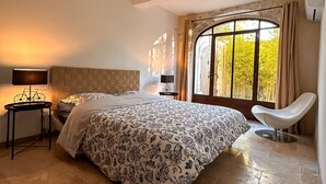 Una camera da letto con un letto grande, un comodino con una lampada, una sedia e una finestra con tende.