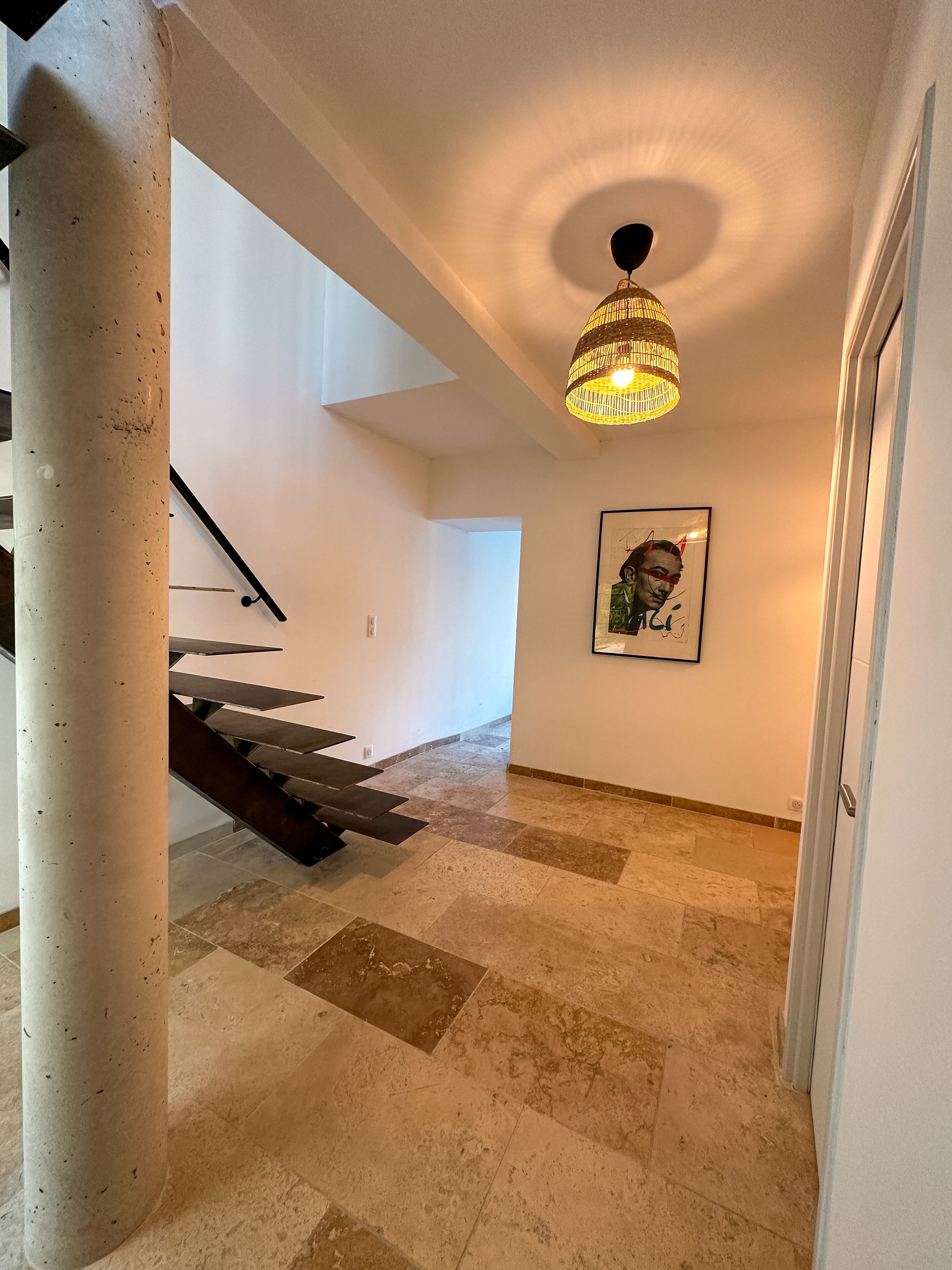 A hallway with a staircase, a hanging light fixture, and a framed picture on the wall.