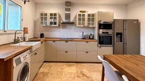 Una cucina moderna con elettrodomestici integrati, lavatrice e zona pranzo con tavolo in legno e sedie bianche.