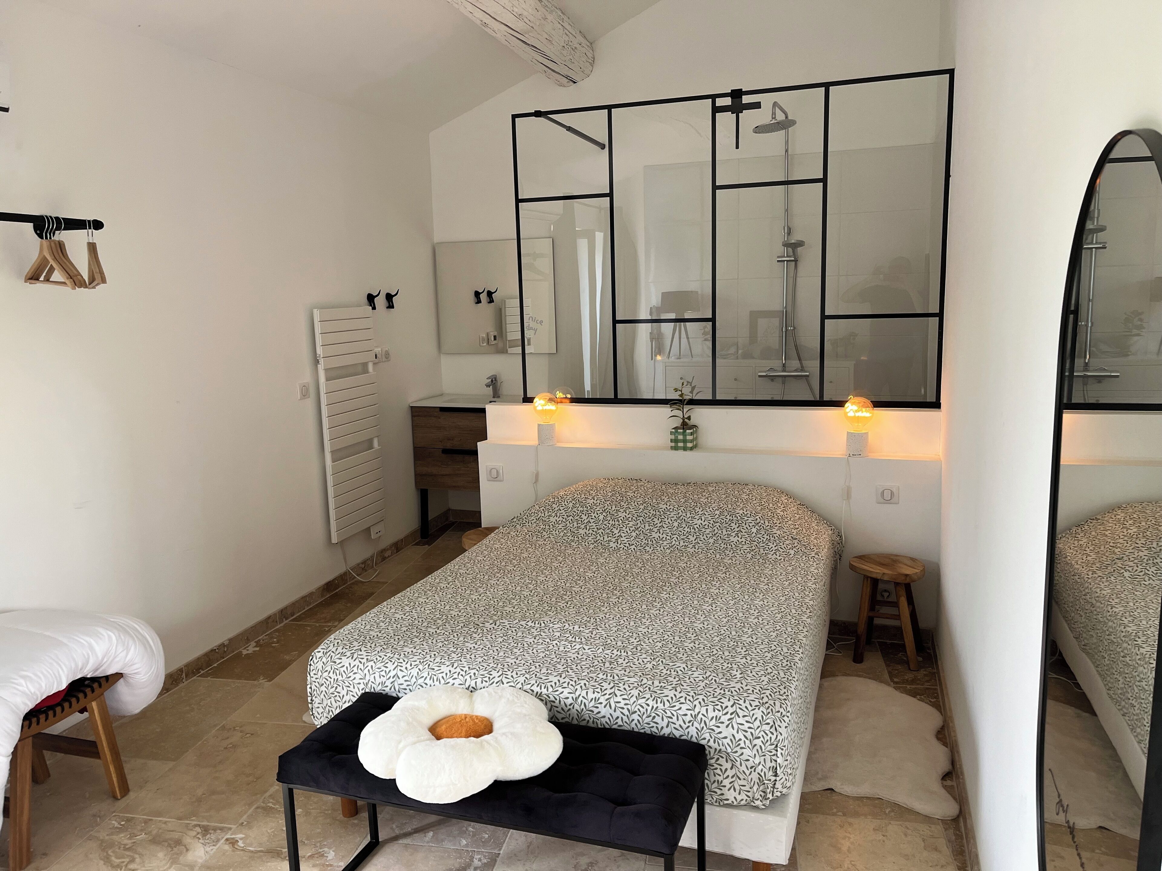 Un dormitorio con cama, mesitas de noche, un espejo, un radiador y una ventana.