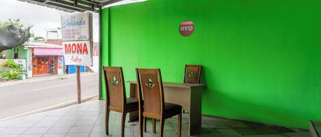 A green wall with a sign for 'OYO' and a 'MONA Salon' sign. There are two wooden chairs and a table in front of the wall.