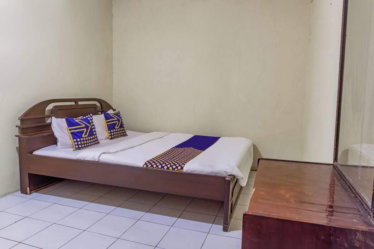 Una cama individual con estructura de madera y colchón blanco, acompañada de dos almohadas con diseños azules y amarillos.