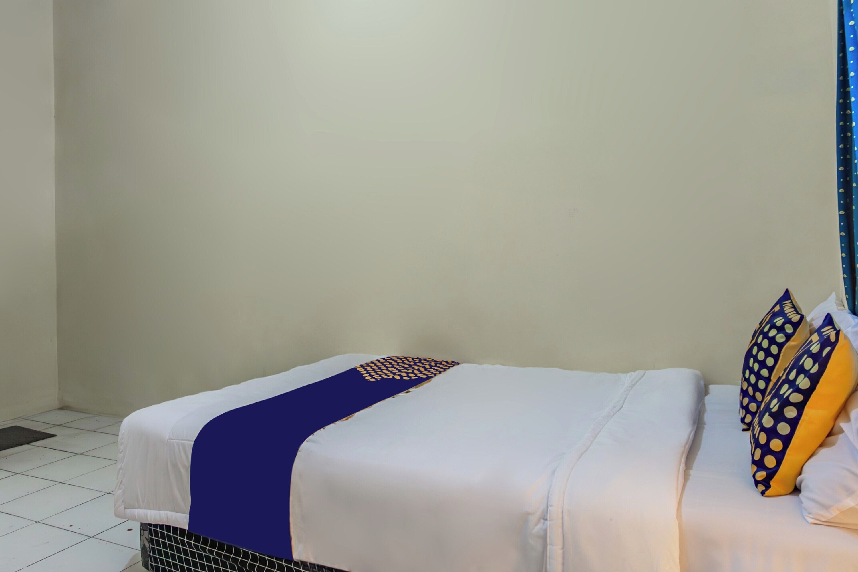 Uma cama de solteiro com colchão branco, almofadas estampadas em azul e amarelo e manta azul.
