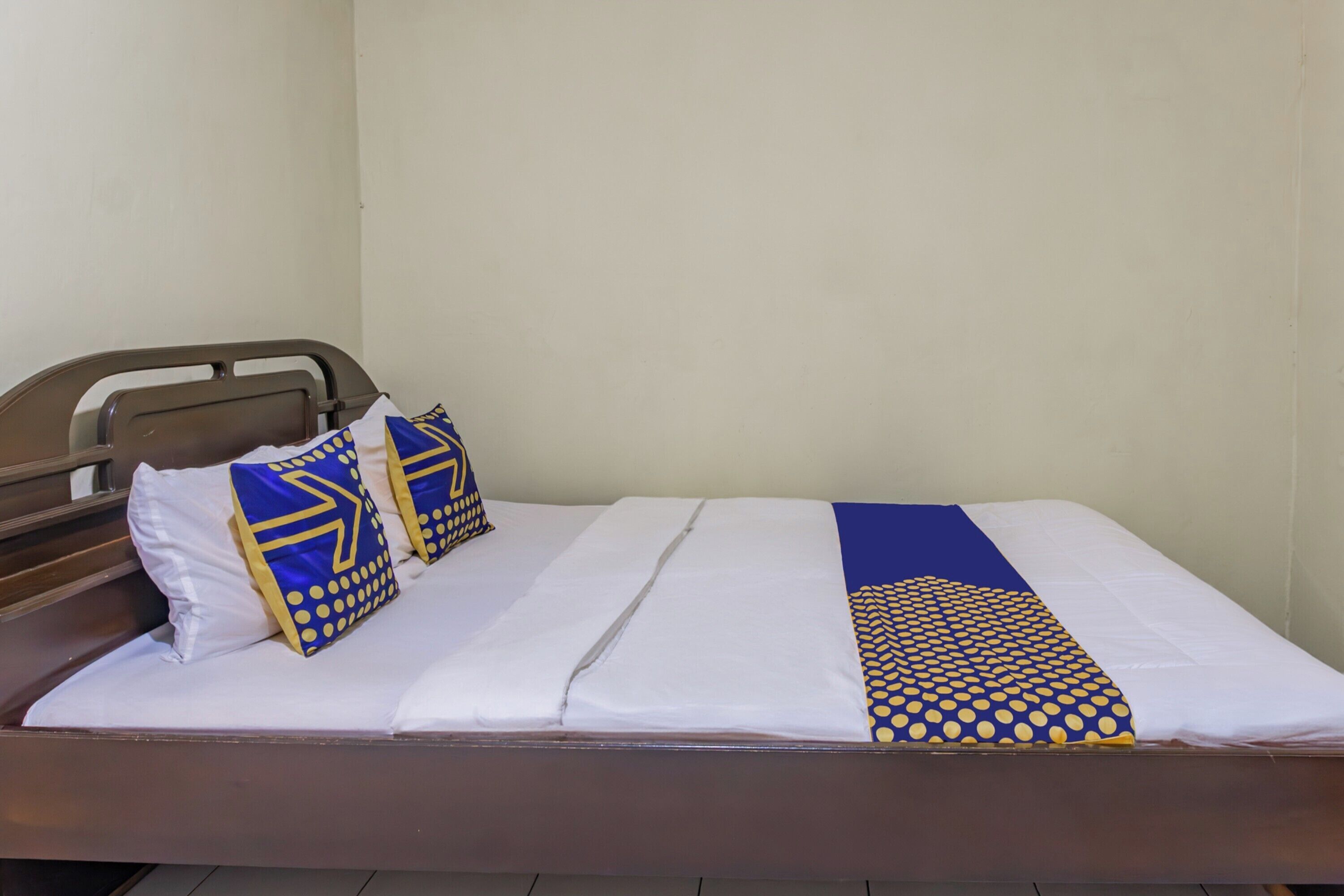 A bed with a white mattress, two pillows with blue and yellow patterns, and a blue and yellow blanket.