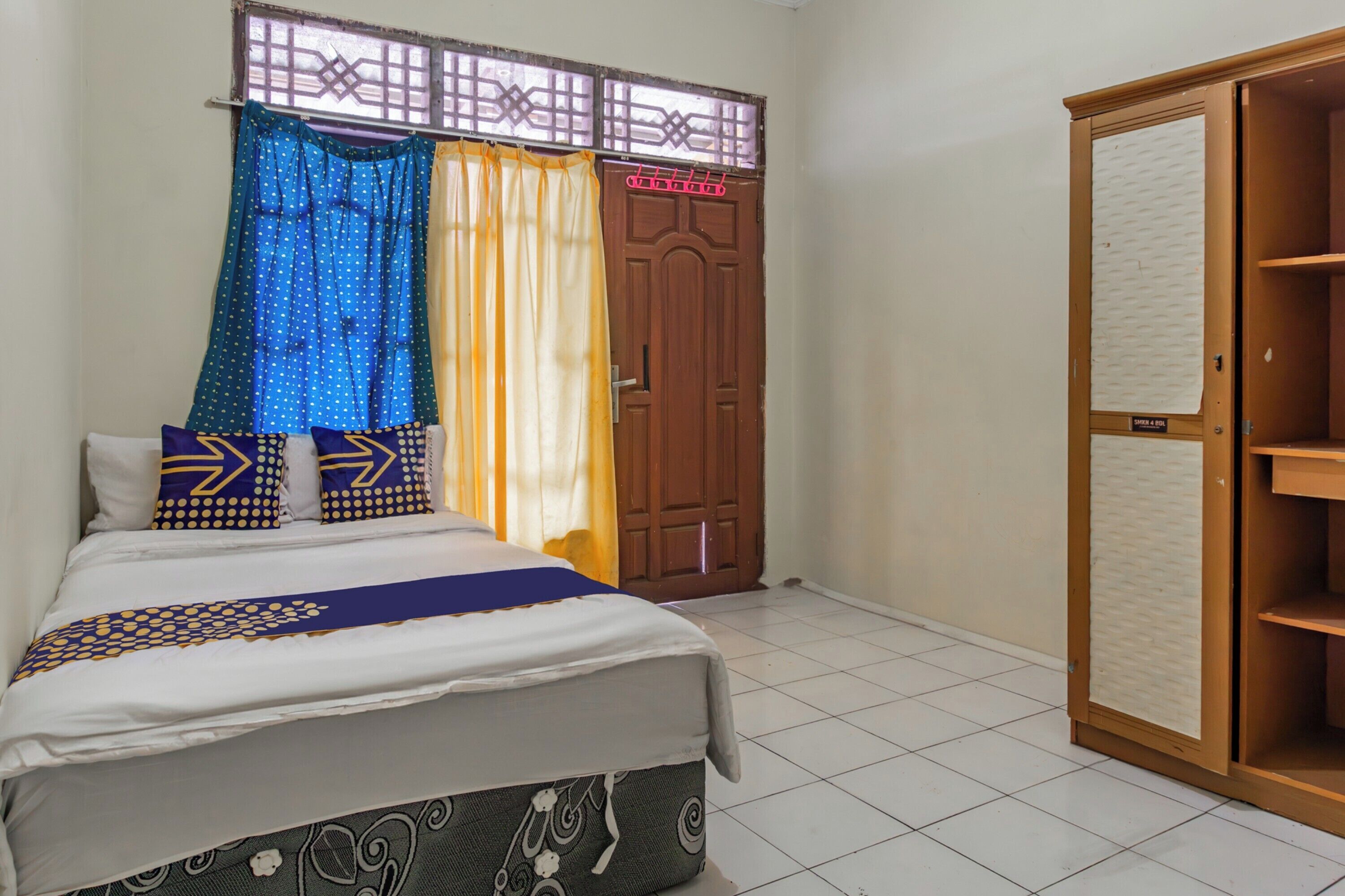 A bedroom with a bed, curtains, a wardrobe, and a window.