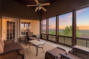 A covered outdoor area with wicker furniture, a ceiling fan, and large windows offering a view of the landscape. - Renovated Game Room! 3 pools, Ozark View, & Close to SDC! (Branson West)