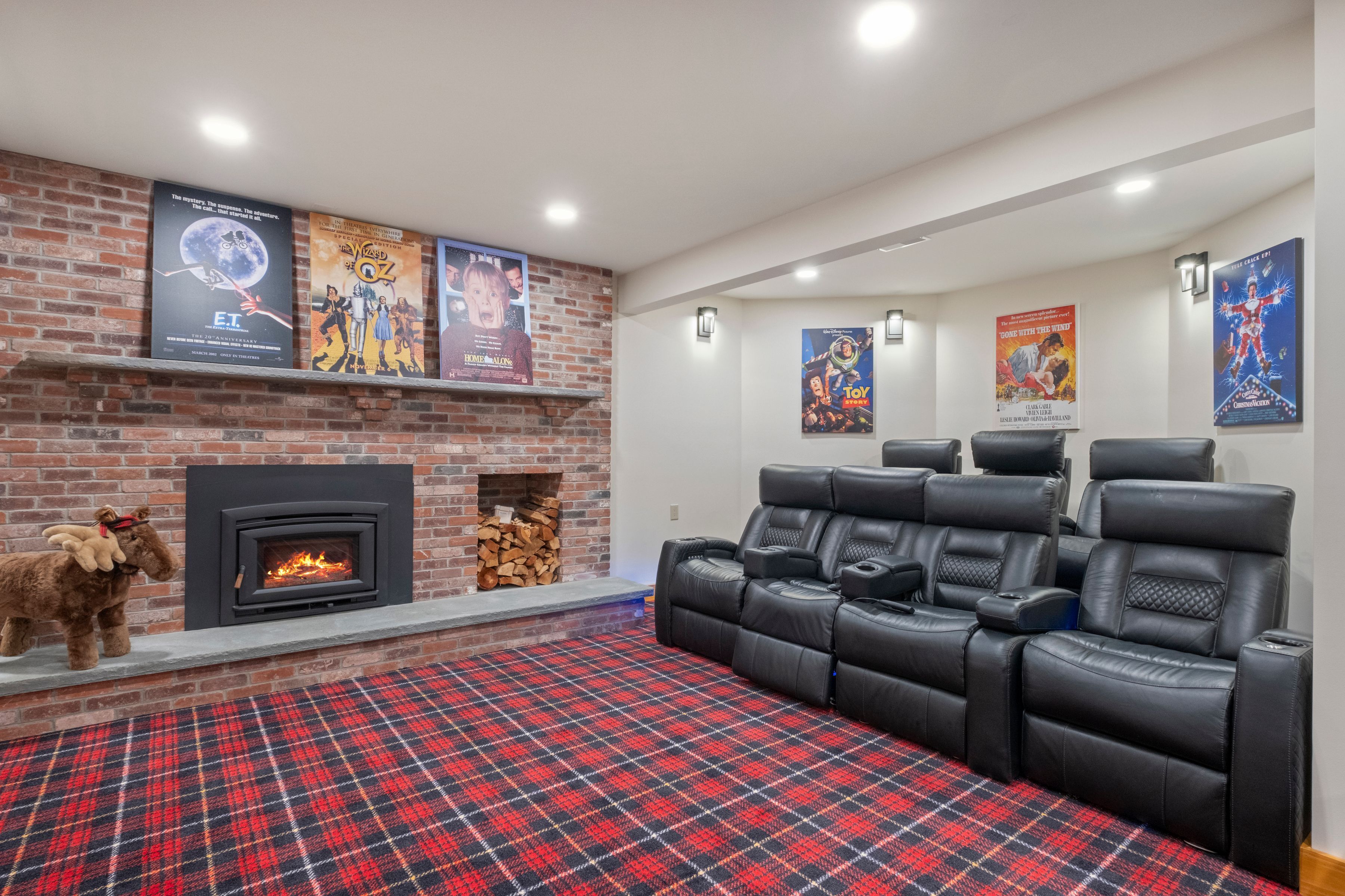 A home theater room with a fireplace, a large red plaid carpet, and black leather recliners.