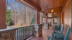 Een houten terras met stenen balustrades, groene Adirondack-stoelen en een stenen open haard.