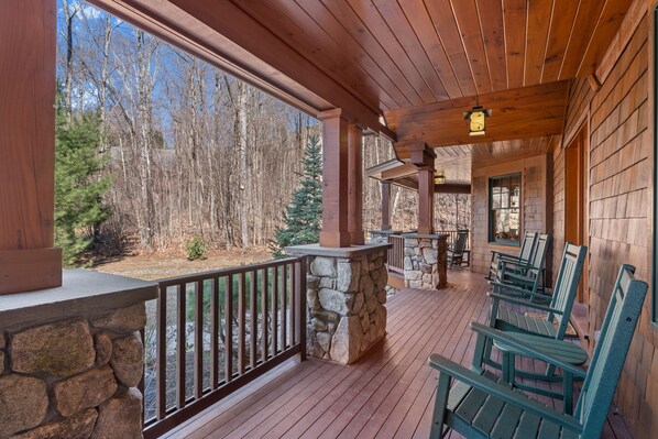 Une terrasse en bois avec des rampes en pierre, des fauteuils Adirondack verts et une cheminée en pierre.