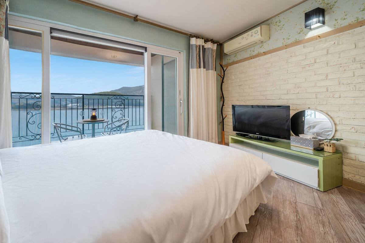 Habitación de hotel con balcón, cama, televisión y una pequeña mesa con sillas.