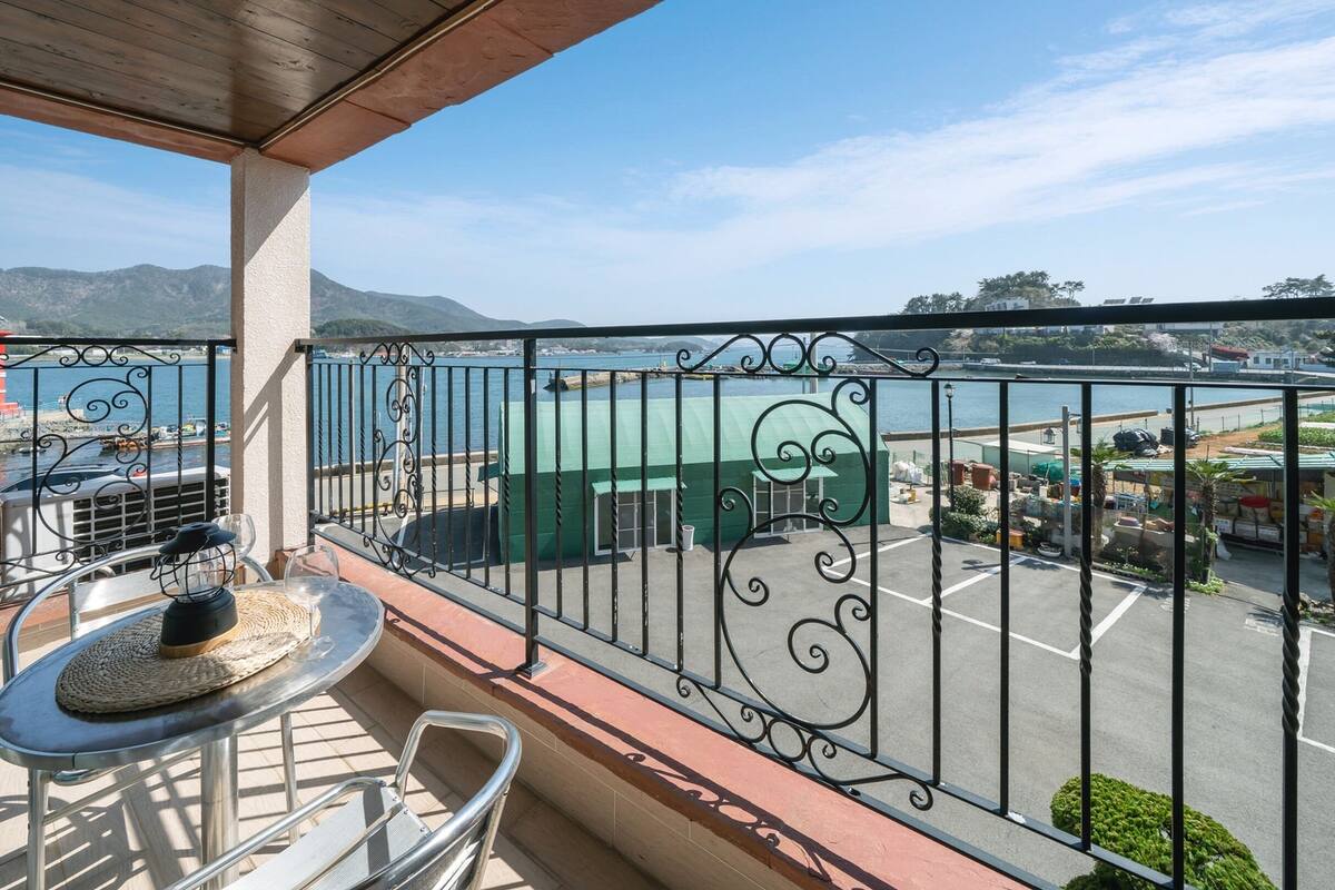 Un balcón con vista al puerto, una mesa con un vaso y una silla.